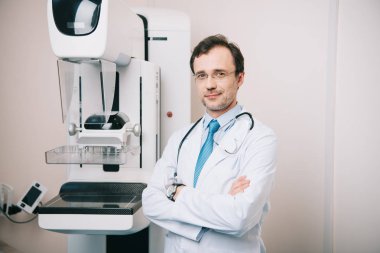 gülümseyen doktor x-ray makinesi yakınında çapraz kolları ile ayakta ve kamera bakarak