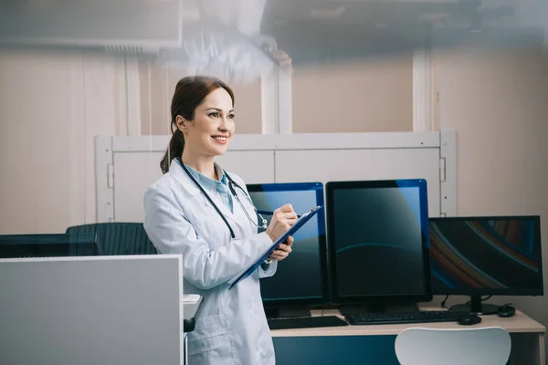Pretty Young Doctor White Coat Smiling While Writing Clipboard — Stock Photo, Image