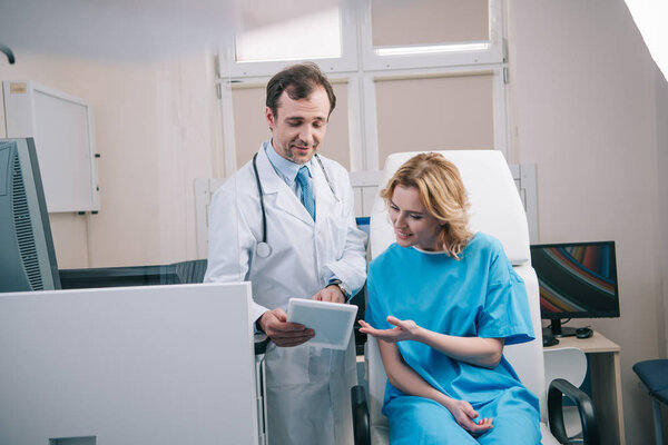 selective focus of handsome doctor showing digital tablet to smiling woman