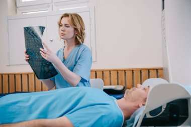 ct tarayıcı yatağında yatan hastanın yanında x-ray tanısı inceleyen özenli doktor
