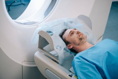 adult handsome man lying on ct scan bed during tomography test  clipart