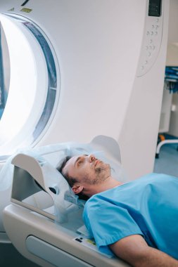 handsome man lying on ct scanner bed while having tomography test clipart