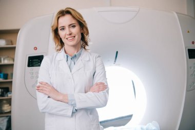 neşeli radyolog bilgisayarlı tomografi tarayıcı yakınında çapraz kolları ile ayakta ve kamera bakarak