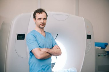 gülümseyen radyolog çapraz kolları ile bilgisayarlı tomografi tarayıcı yanında duran ve kamera bakarak