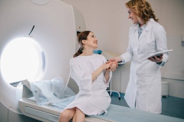 bilgisayarlı tomografi tarayıcı yatakta oturan mutlu kadın ile el ele gülümseyen radyolog