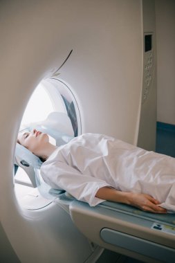 Radyoloji testi sırasında kapalı gözlü bir kadın bilgisayarlı tomografi tarama masasında yatıyor.