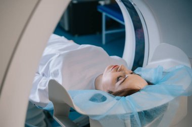 Tomografi taraması sırasında tomografi yatağında yatan genç bir kadın.