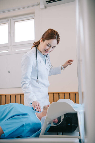 selective focus of pretty smiling radiologist preparing patient for scanning in mri machine