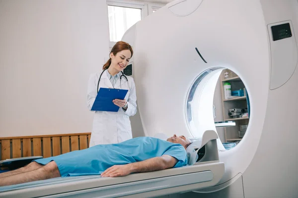 Belo Radiologista Segurando Prancheta Enquanto Prepara Paciente Para Tomografia — Fotografia de Stock