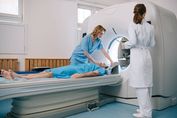 radiologist in white coat standing near ct scanner while nurse preparing patient for diagnostics