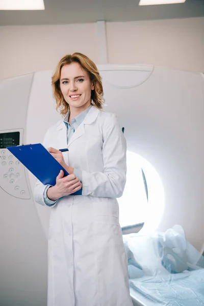Smiling Radiographer Writing Clipboard Looking Camera While Standing Mri Machine — Stock Photo, Image
