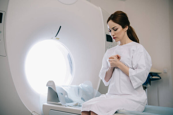 beautiful woman praying with closed eyes while sitting on mri scanner bed in hospital