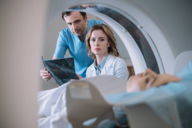 selective focus of doctors holding x-ray diagnosis and looking at woman during diagnostics on computed tomography scanner