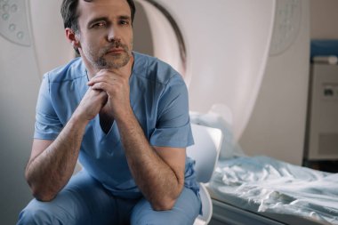 hastanede bilgisayarlı tomografi tarayıcı yakınında oturan ve kamera bakarak pensive doktor