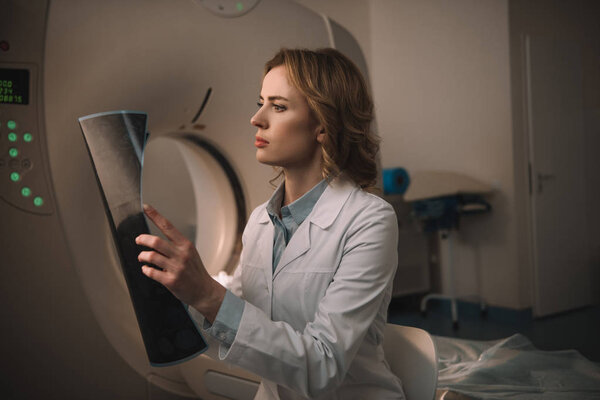 thoughtful radiologist examining x-ray diagnosis while sitting near ct scanner 