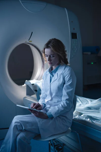 坐在计算机断层扫描器附近使用数字平板电脑的周到放射科医生 — 图库照片