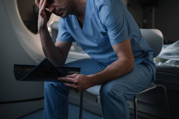 tired radiologist holding x-ray diagnosis while sitting near computed tomography scanner in hospital 