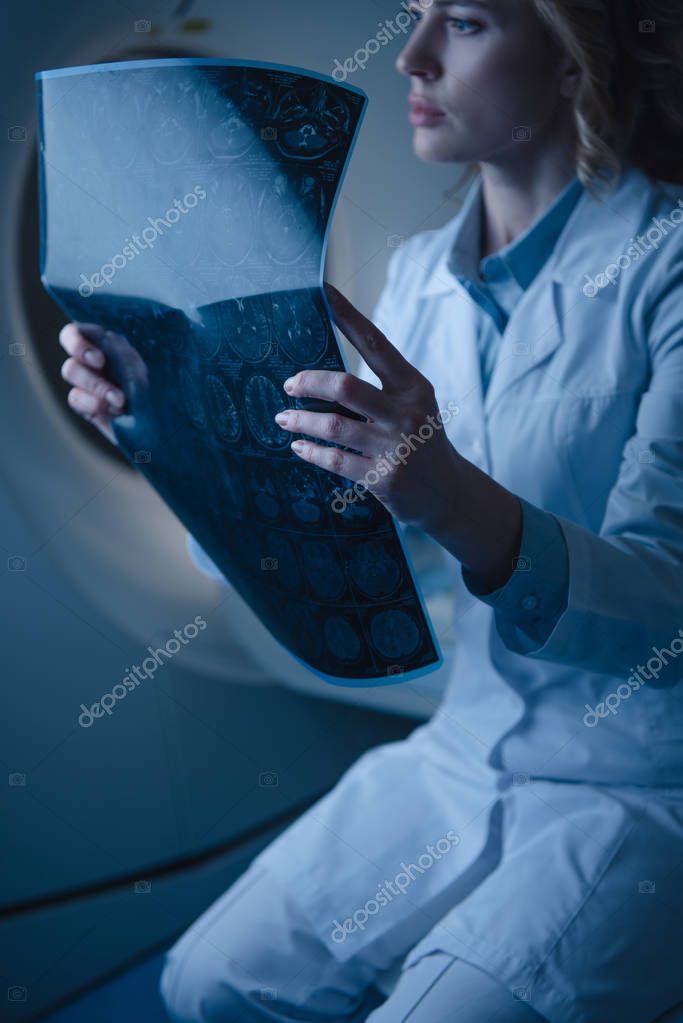 Thoughtful doctor holding x-ray diagnosis while sitting at computed tomography scanner