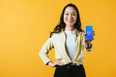 Kiev, Ukrayna - 16 Nisan 2019: shazam uygulaması ile akıllı telefon gösteren gülümseyen asyalı kız, sarı izole