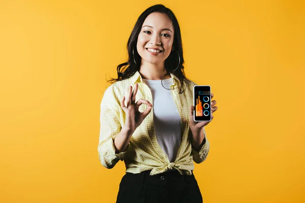 Sorridente Ragazza Asiatica Mostrando Segno Smartphone Con Infografica Isolato Giallo — Foto Stock