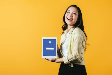 Kiev, Ukrayna - 16 Nisan 2019: facebook uygulaması ile dijital tablet gösteren gülümseyen asyalı kız, sarı izole