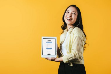 Gülümseyen asyalı kız instagram uygulaması ile dijital tablet gösteren, sarı izole