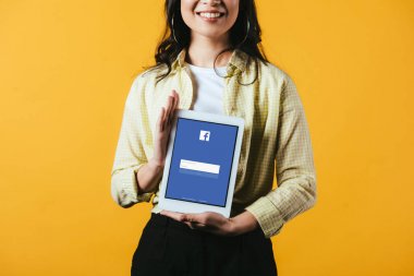 Kiev, Ukrayna - 16 Nisan 2019: facebook uygulaması ile dijital tablet gösteren gülümseyen kız kırpılmış görünümü, sarı izole