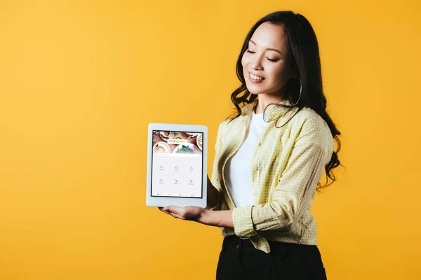 乌克兰 2019年4月16日 美丽的亚洲女孩显示数字平板电脑与四方形应用程序 隔离在黄色 — 图库照片