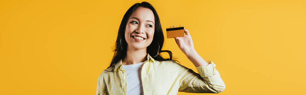 smiling asian woman holding credit card, isolated on yellow