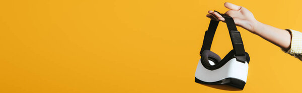 partial view of woman holding Virtual reality headset, isolated on yellow