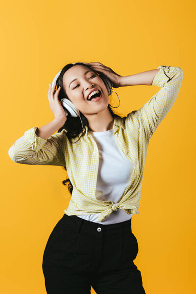 beautiful asian girl singing and listening music with headphones, isolated on yellow