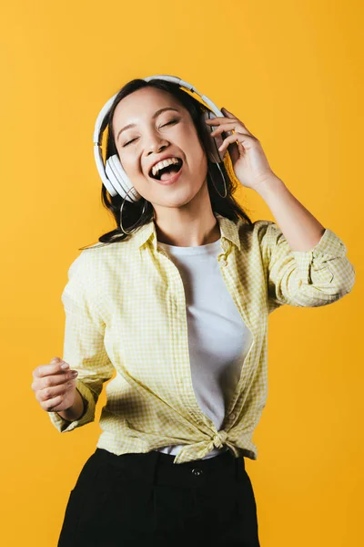 欢快的亚洲妇女唱歌和听音乐与耳机 隔离在黄色 — 图库照片