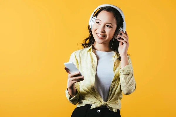 Glimlachend Aziatisch Meisje Luisteren Muziek Met Koptelefoon Smartphone Geïsoleerd Geel — Stockfoto