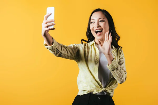 黄色で隔離されたスマートフォンで手を振り ビデオ通話を行う興奮したアジアの女の子 — ストック写真