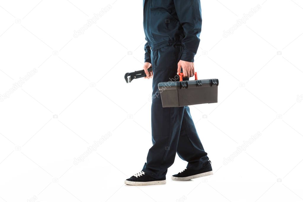 cropped view of plumber in overalls holding toolbox and adjustable wrench isolated on white