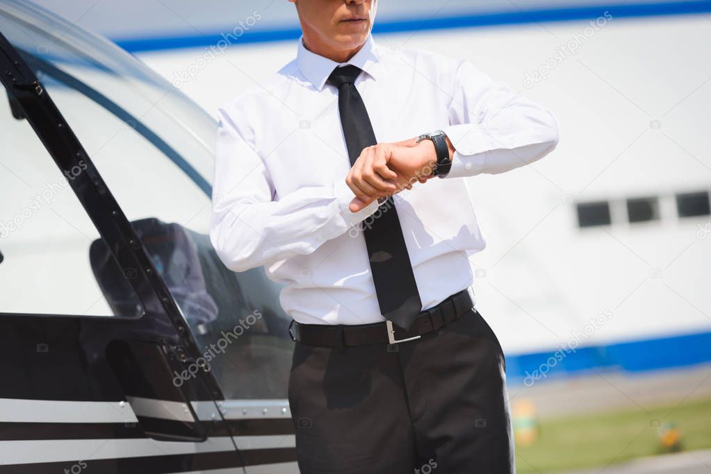 cropped view of Pilot in formal wear adjusting watch near helicopter