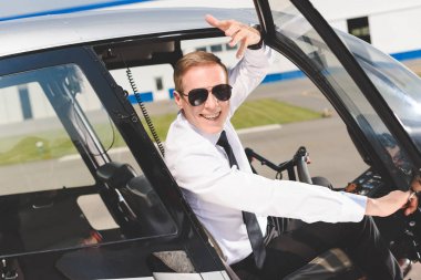 güneş gözlüğü ve resmi aşınma ve helikopter kabininde oturan gülümseyen pilot
