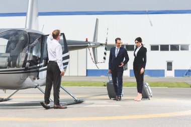 business partners in formal wear with suitcases near pilot and helicopter clipart