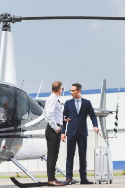 Helikopter yanında bavul ile resmi giyim ve işadamı pilot