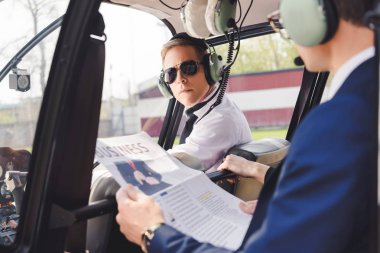 Pilot in headset and businessman with newspaper in helicopter cabin clipart