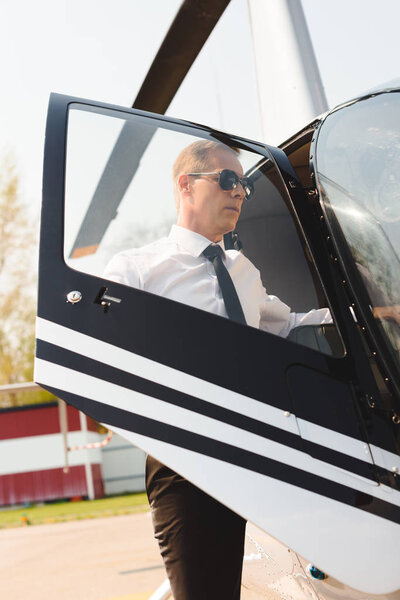 mature Pilot in formal wear and sunglasses opening door of helicopter