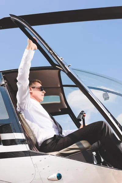穿着太阳镜和正式的衣服的帅气飞行员坐在直升机机舱里 — 图库照片