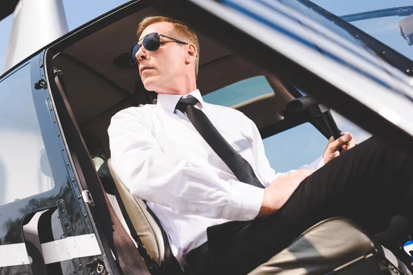 güneş gözlüğü ve resmi aşınma helikopter kabin oturan yakışıklı pilot düşük açı görünümü