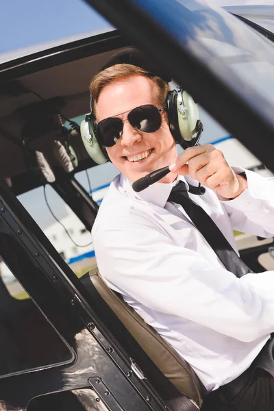 Przystojny Uśmiechnięty Pilot Okulary Przeciwsłoneczne Słuchawki Siedzi Kabinie Śmigłowca — Zdjęcie stockowe