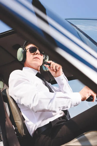 low angle view of Pilot in sunglasses and headset sitting in helicopter cabin