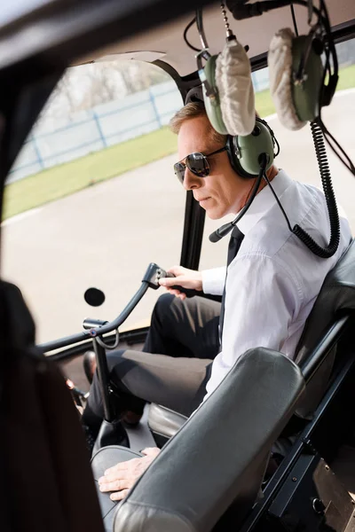 成熟飞行员在正式的磨损和耳机坐在直升机机舱和保持轮 — 图库照片