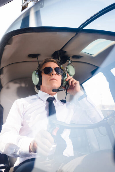 mature Pilot in sunglasses and headset with microphone sitting in helicopter cabin