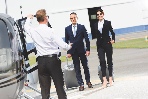 бизнес-партнеры с багажом рядом с пилотом и вертолетом
