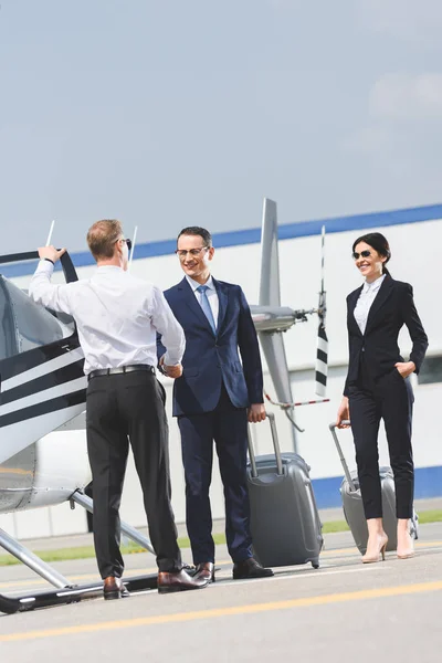 ヘリコプターや実業家の近くでパイロットと握手する荷物を持つビジネスマン — ストック写真