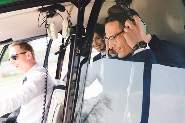 businesspeople in formal wear sitting in helicopter with pilot